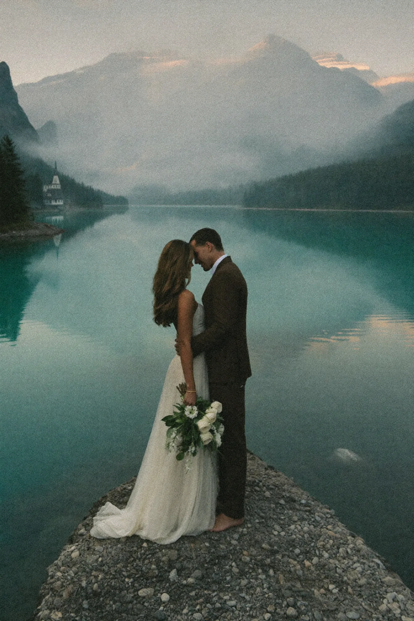 A couple at dawn on the shore of Lake Louise below the Victoria Glacier
