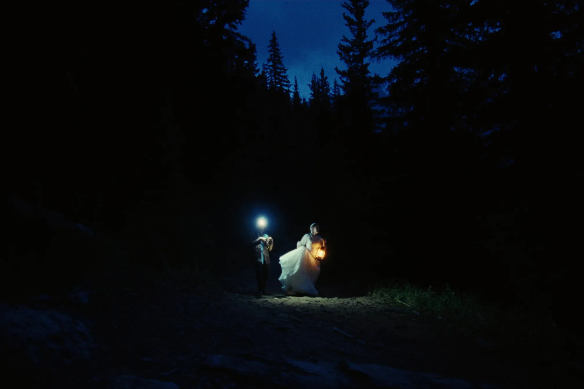 A couple walking a dark forest trail by lantern light before dawn in Banff