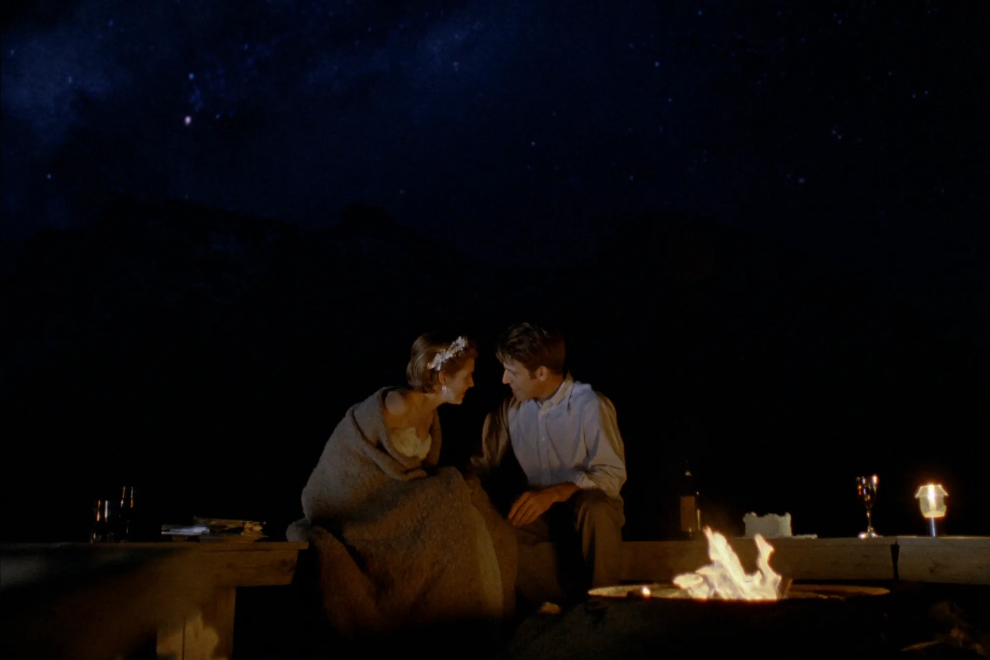 A couple by a fire under the Milky Way on a cabin deck near Revelstoke