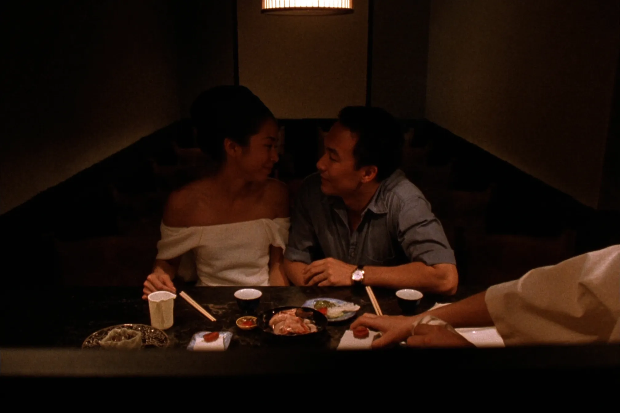 A couple at an intimate izakaya chef's counter in the warm lamplight