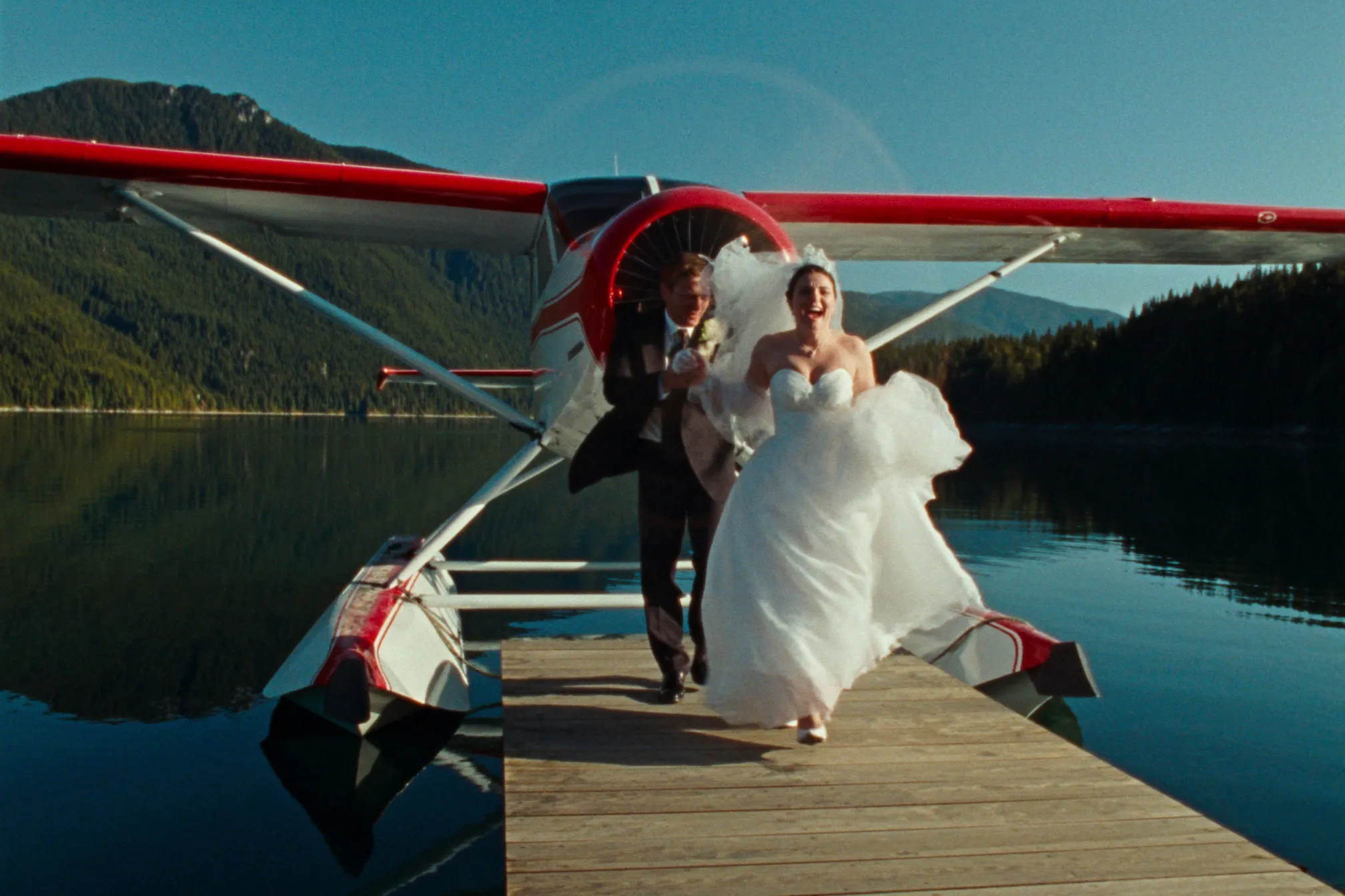 A couple stepping from a floatplane onto a dock in a coastal inlet