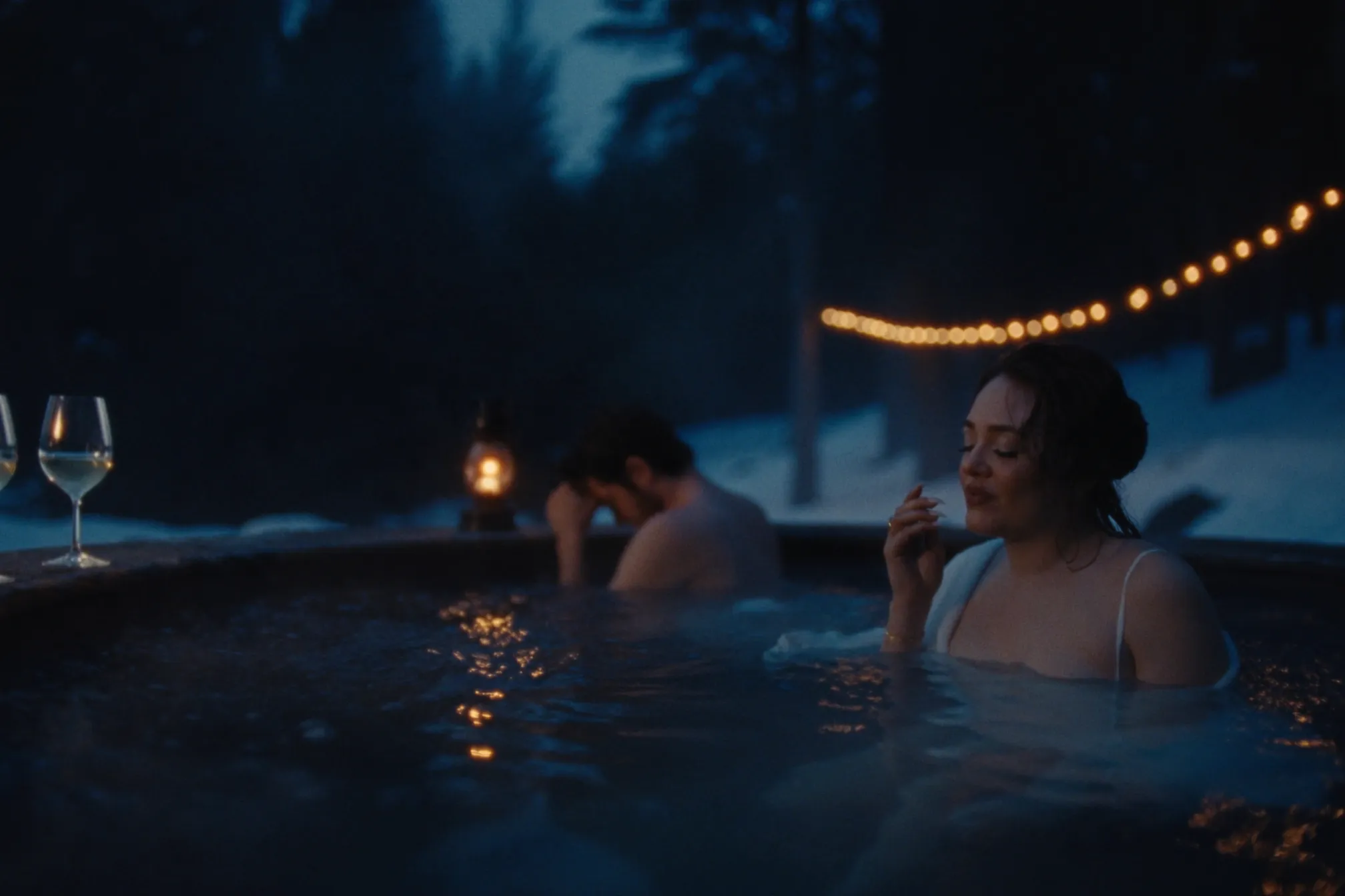 A couple in steaming thermal baths in a snowy cedar forest at dusk