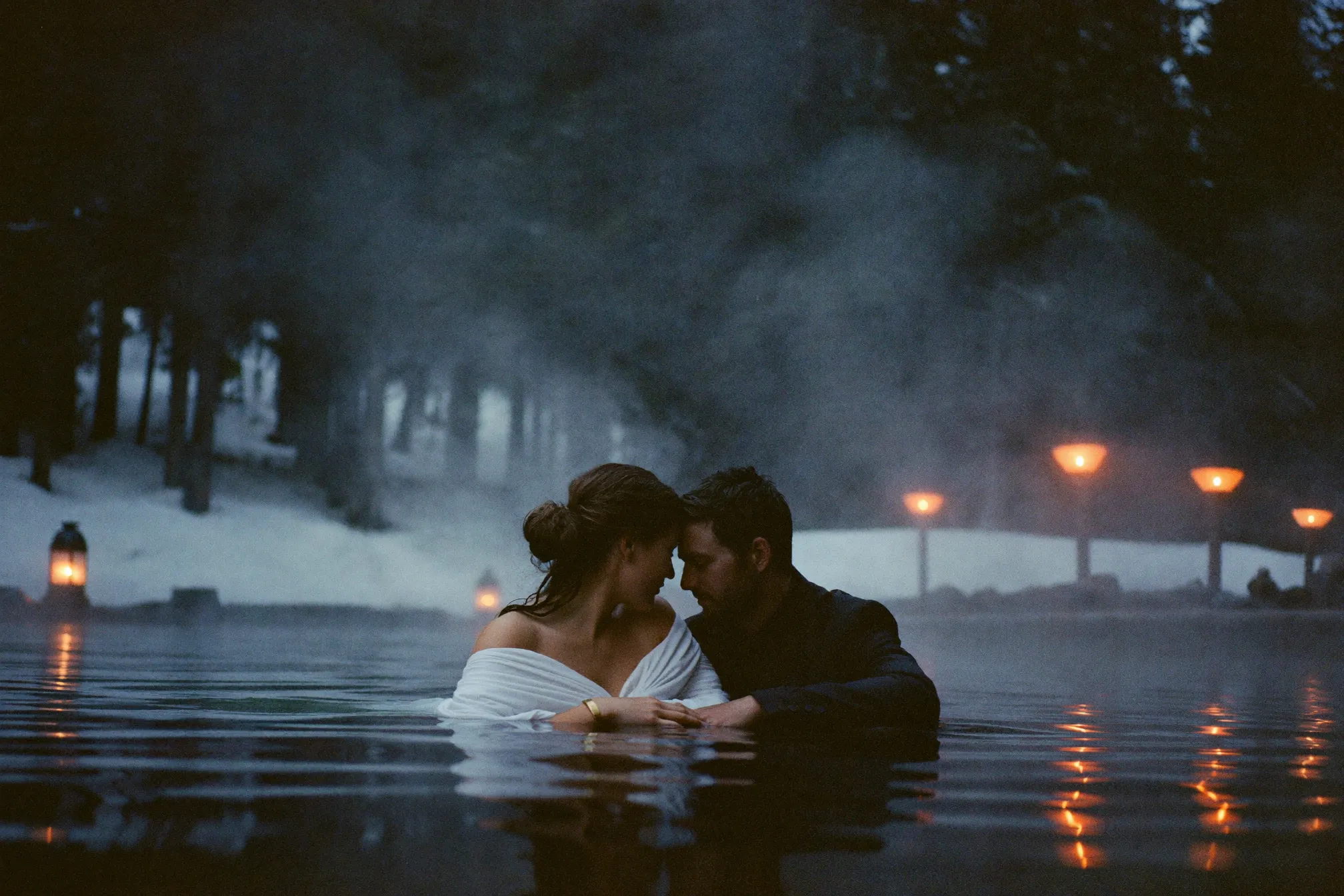 A couple in steaming outdoor thermal baths in a snowy cedar forest