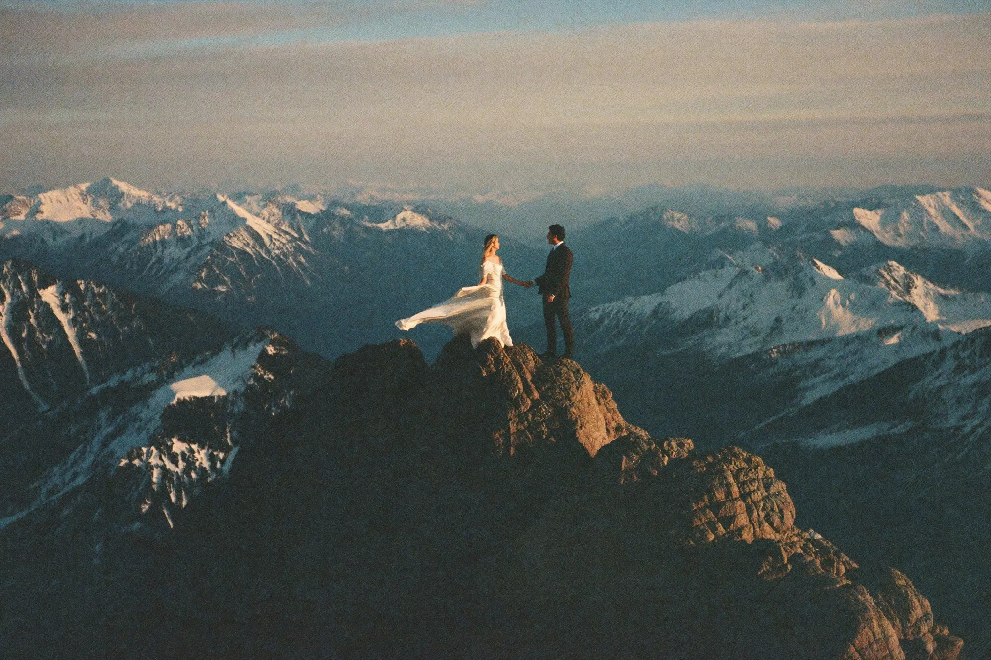 A couple tiny against a vast alpine summit at golden hour